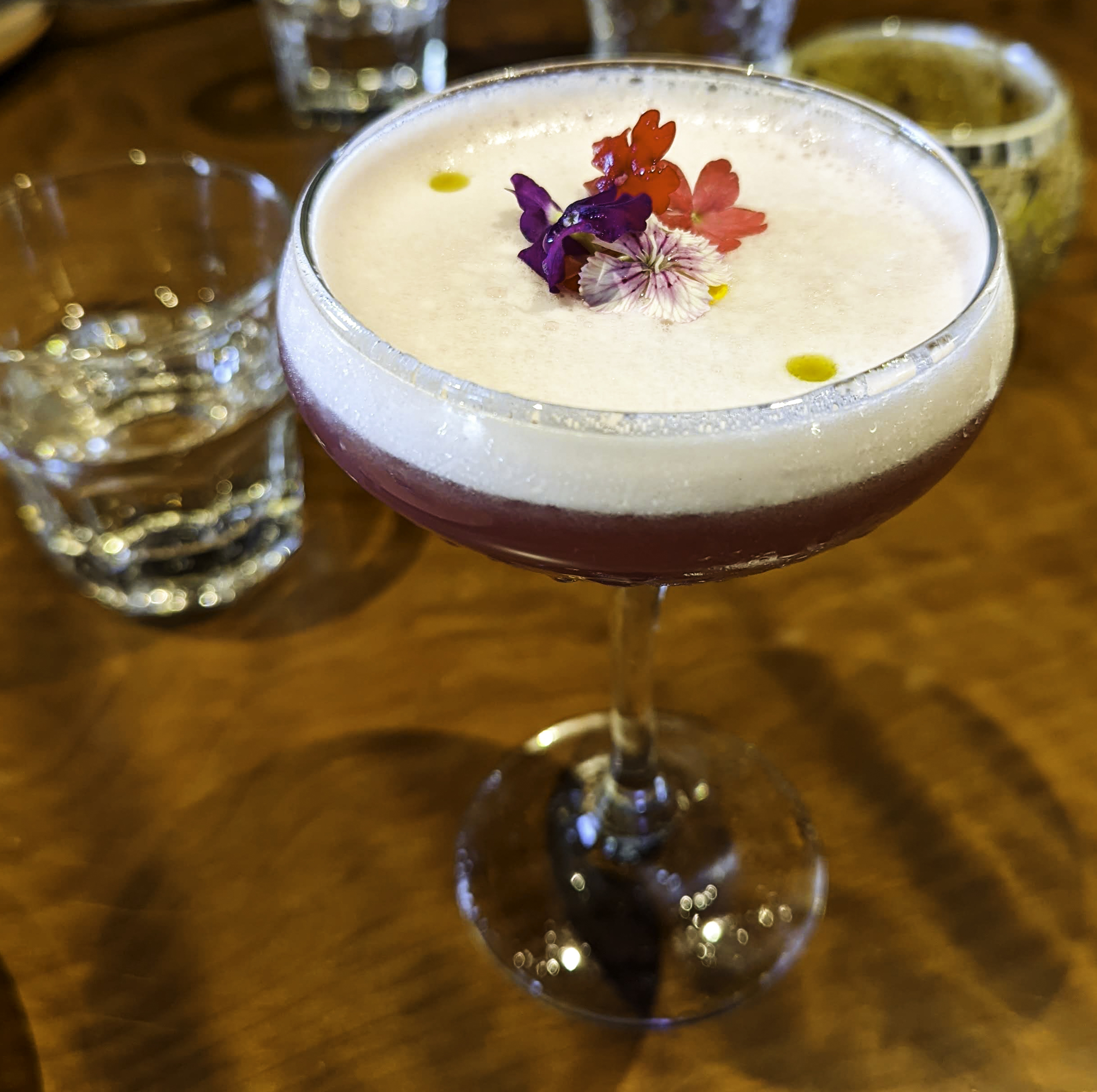 A lavendar cocktail topped with a layer of foam and flowers